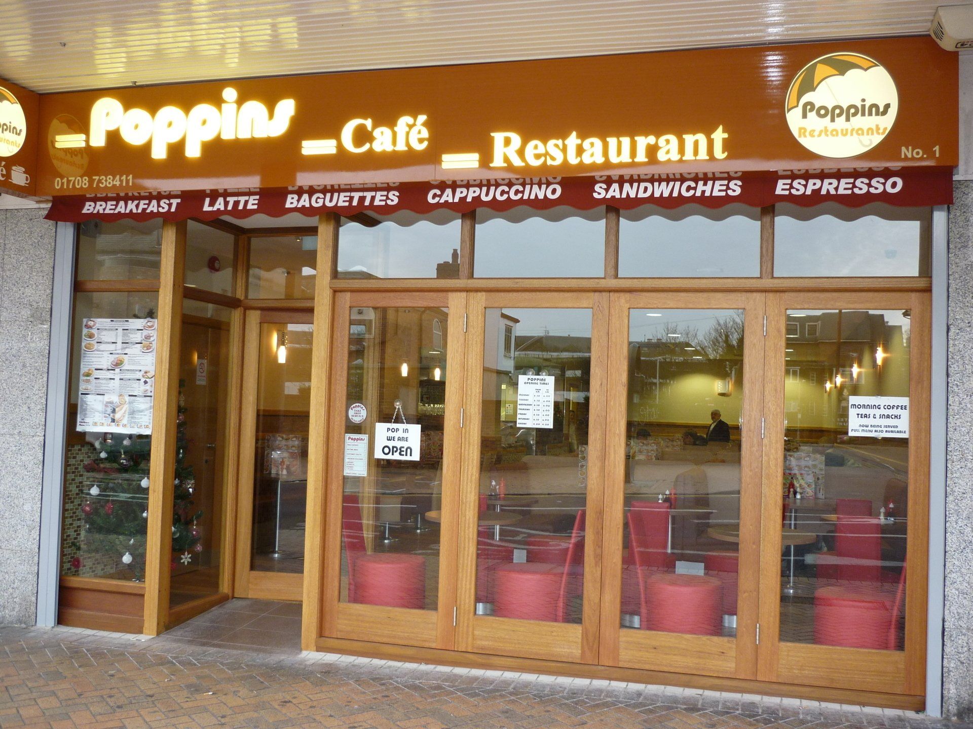 Poppin’ Café restaurant storefront with wooden doors, red tables, and illuminated signage