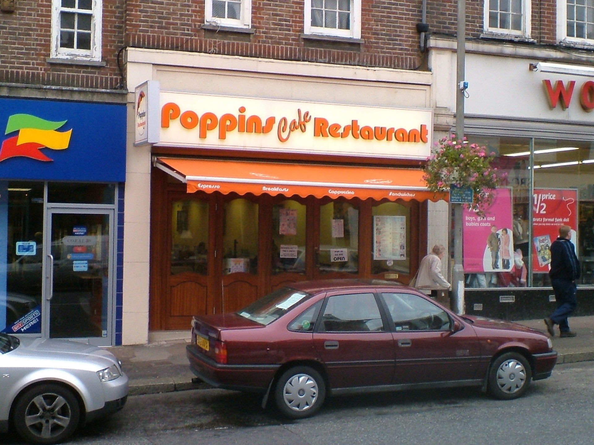 Storefront of Poppin’s Restaurant with orange sign and maroon car parked outside