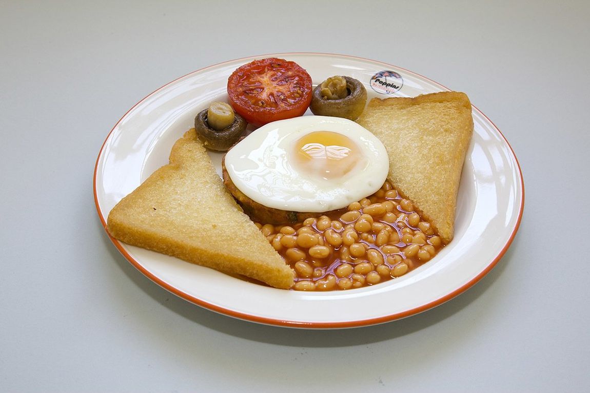 Plate of baked beans with toast triangles, fried egg, tomato halves, and mushrooms on a white dish