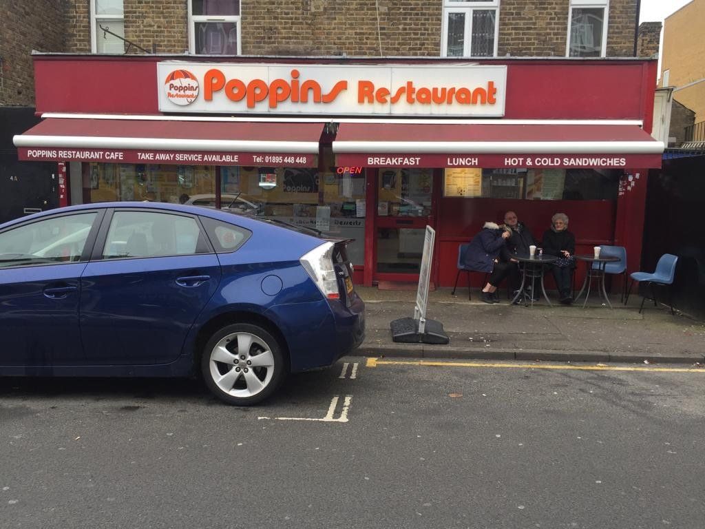 Exterior of Poppin Restaurant with red awning, blue car parked outside, and seated customers on the sidewalk.