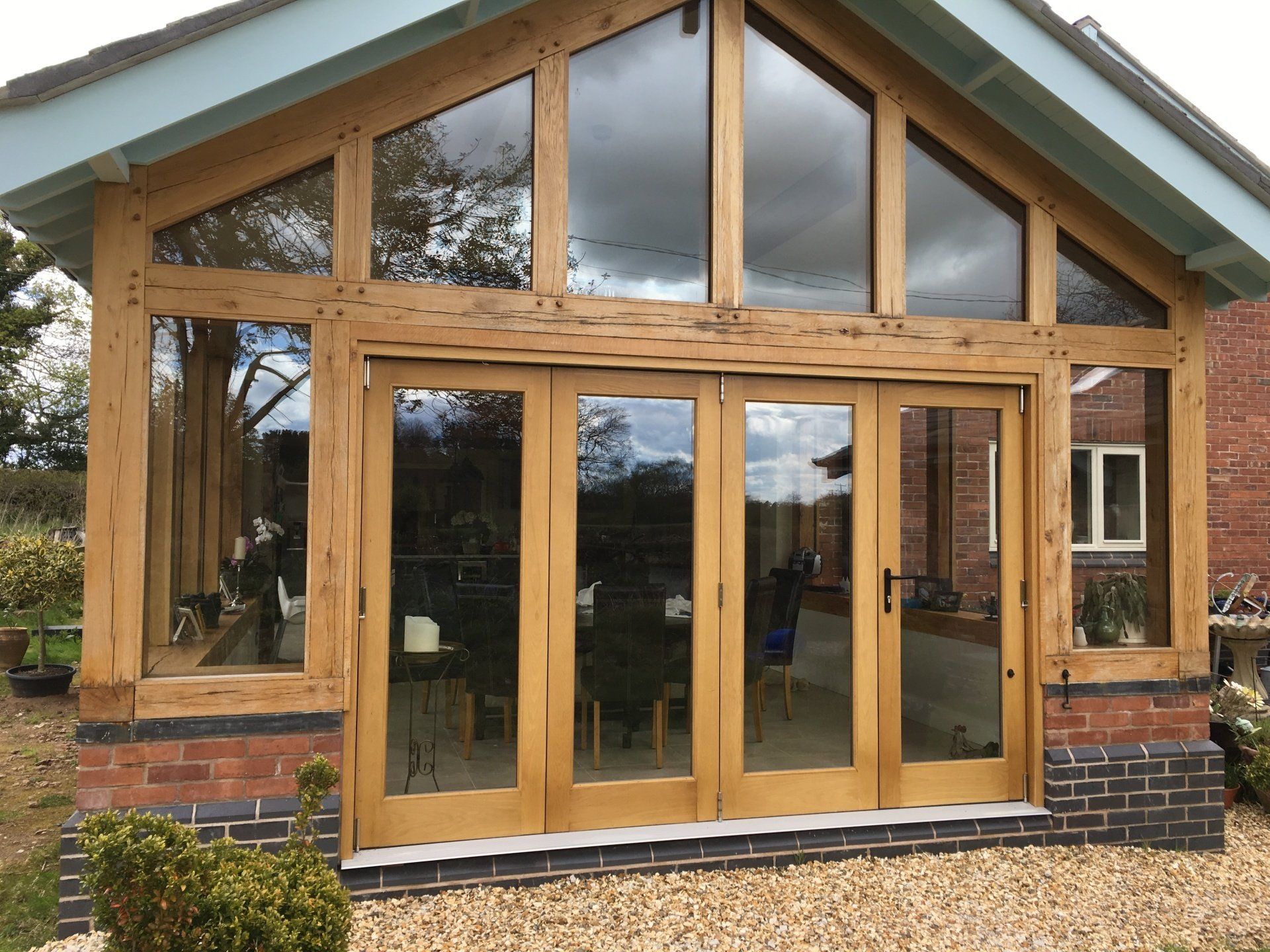 A sunroom with glass doors and windows, set in a brick and wood frame with a light blue roof.