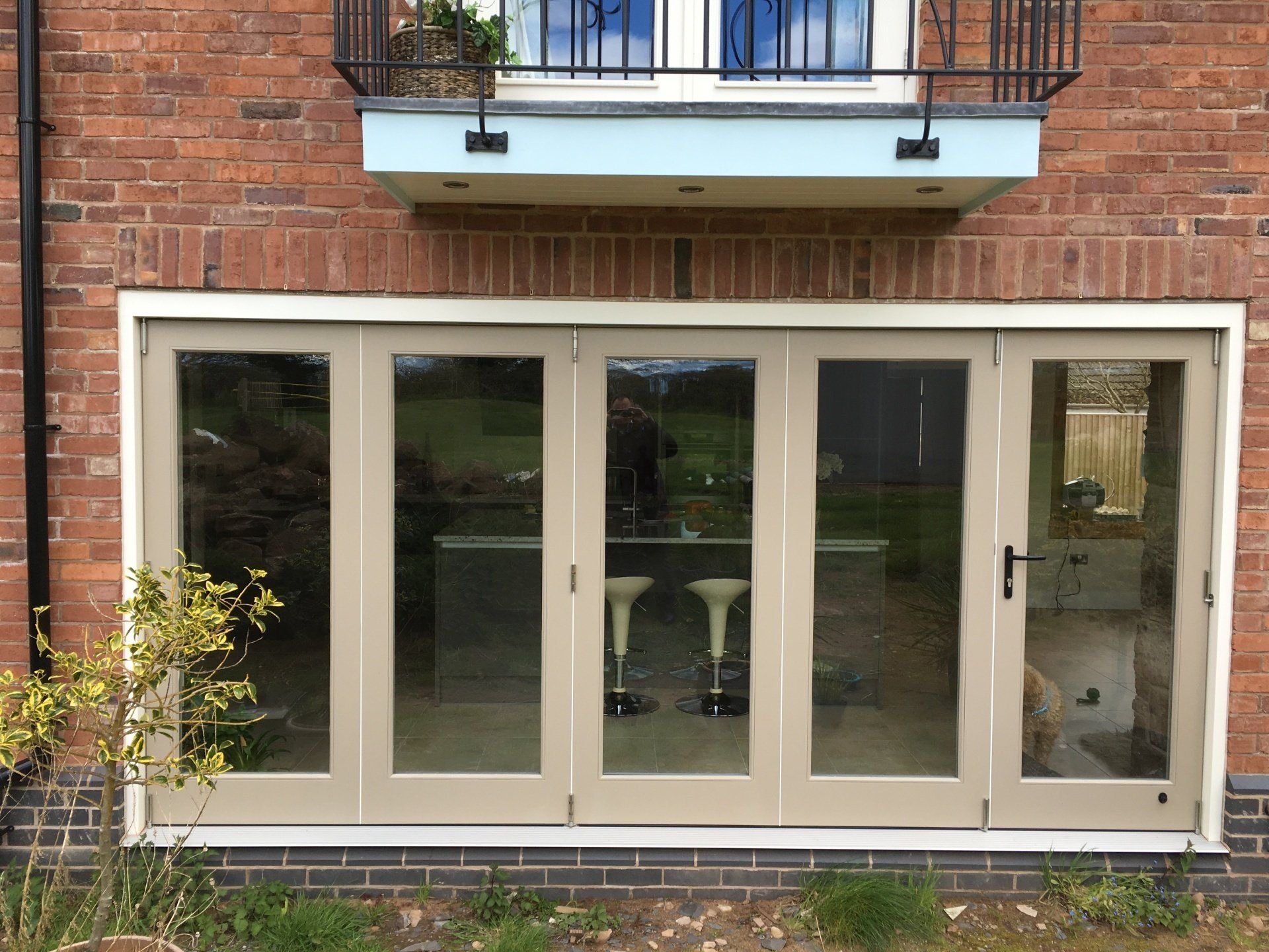 Beige framed glass doors, brick wall, and balcony above.