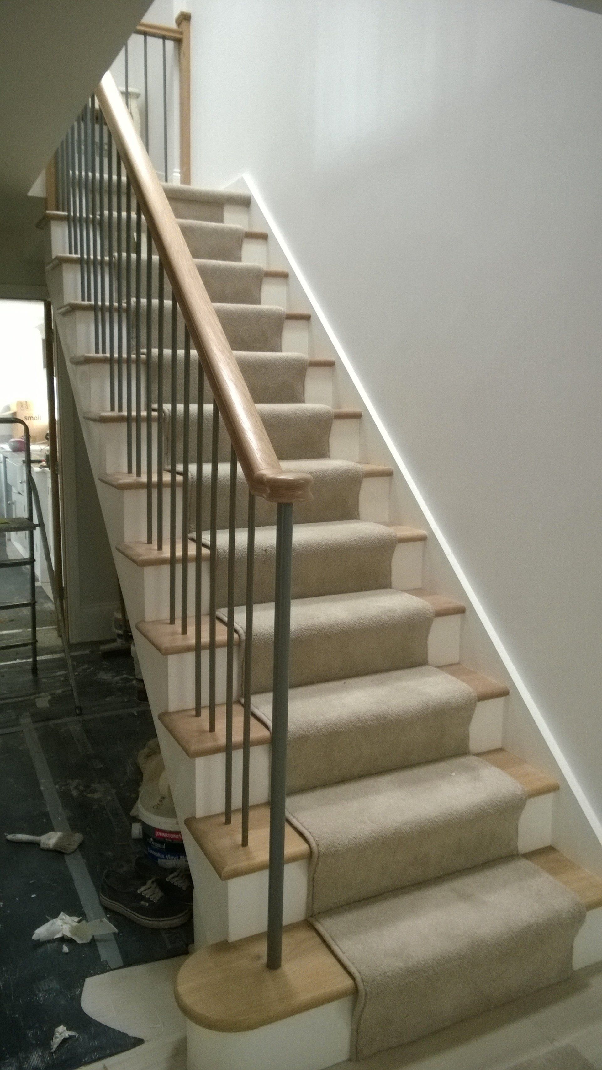 Staircase with carpeted steps, wooden handrail, and metal spindles. Light-colored walls and wooden trim.