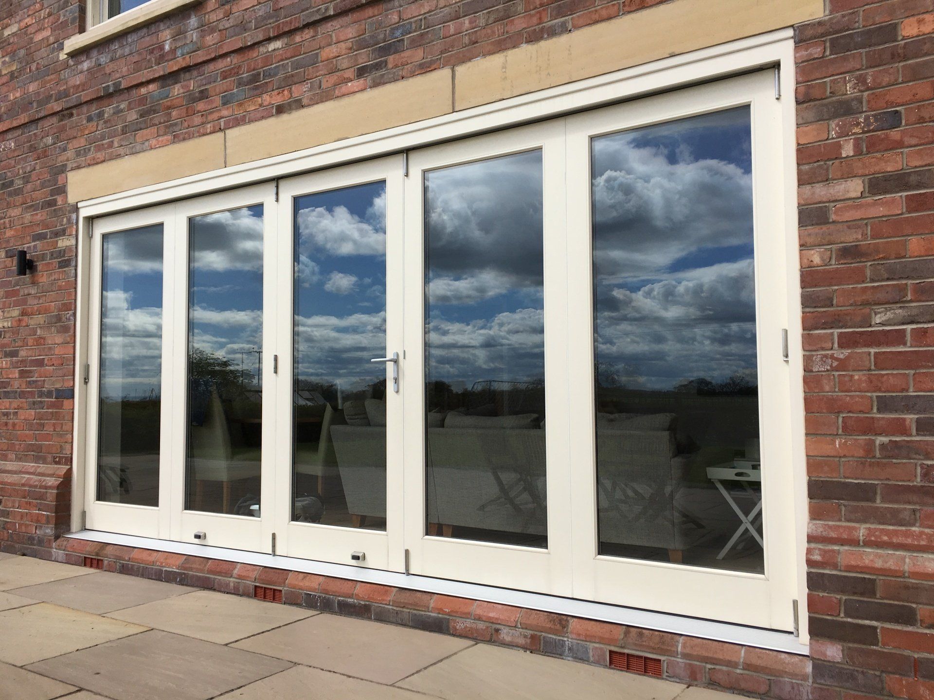 Beige folding glass doors on a brick building, reflecting a cloudy sky.