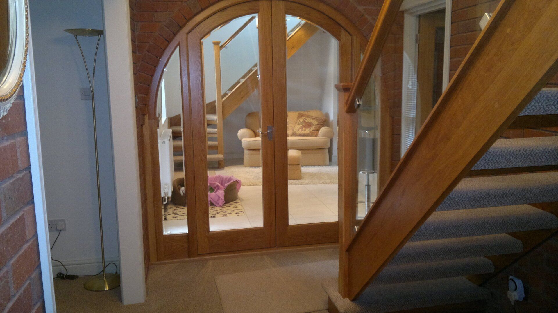 Interior hallway with staircase, arched wooden double doors, and beige walls.