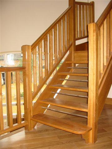 Wooden staircase with railings; light brown wood, ascending indoors.