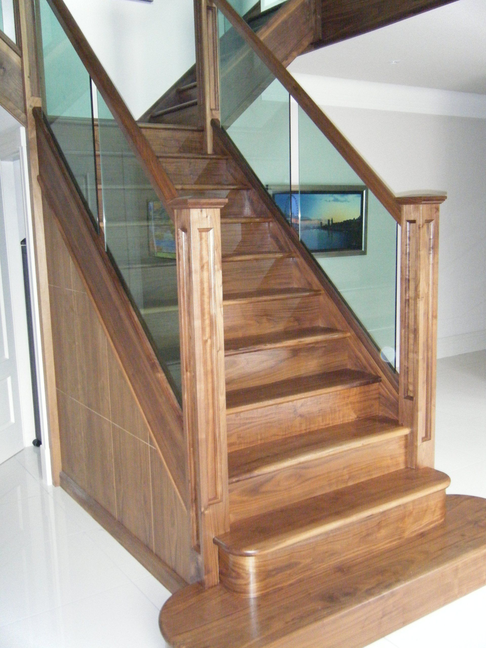 Wooden staircase with glass panels, brown wood, light-colored walls, a painting is visible, natural light.
