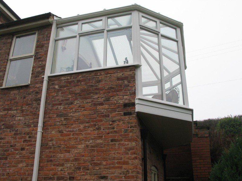 Brick building with a white-framed glass conservatory, overcast sky.