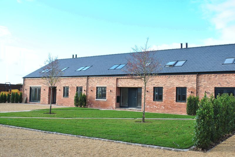 Red brick barn conversion with green lawn, blue sky, and small trees.