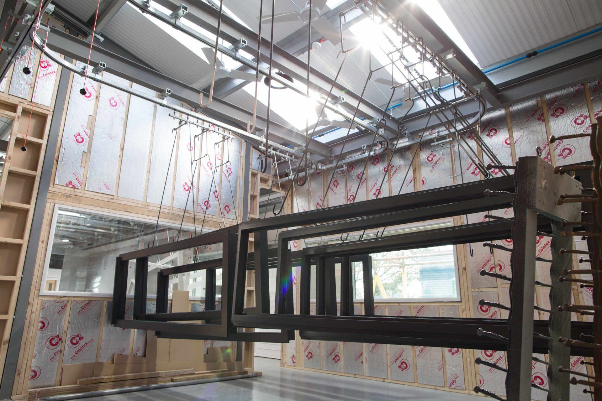 Timber frames hanging inside a workshop with insulation, overhead tracks, and sunlight.