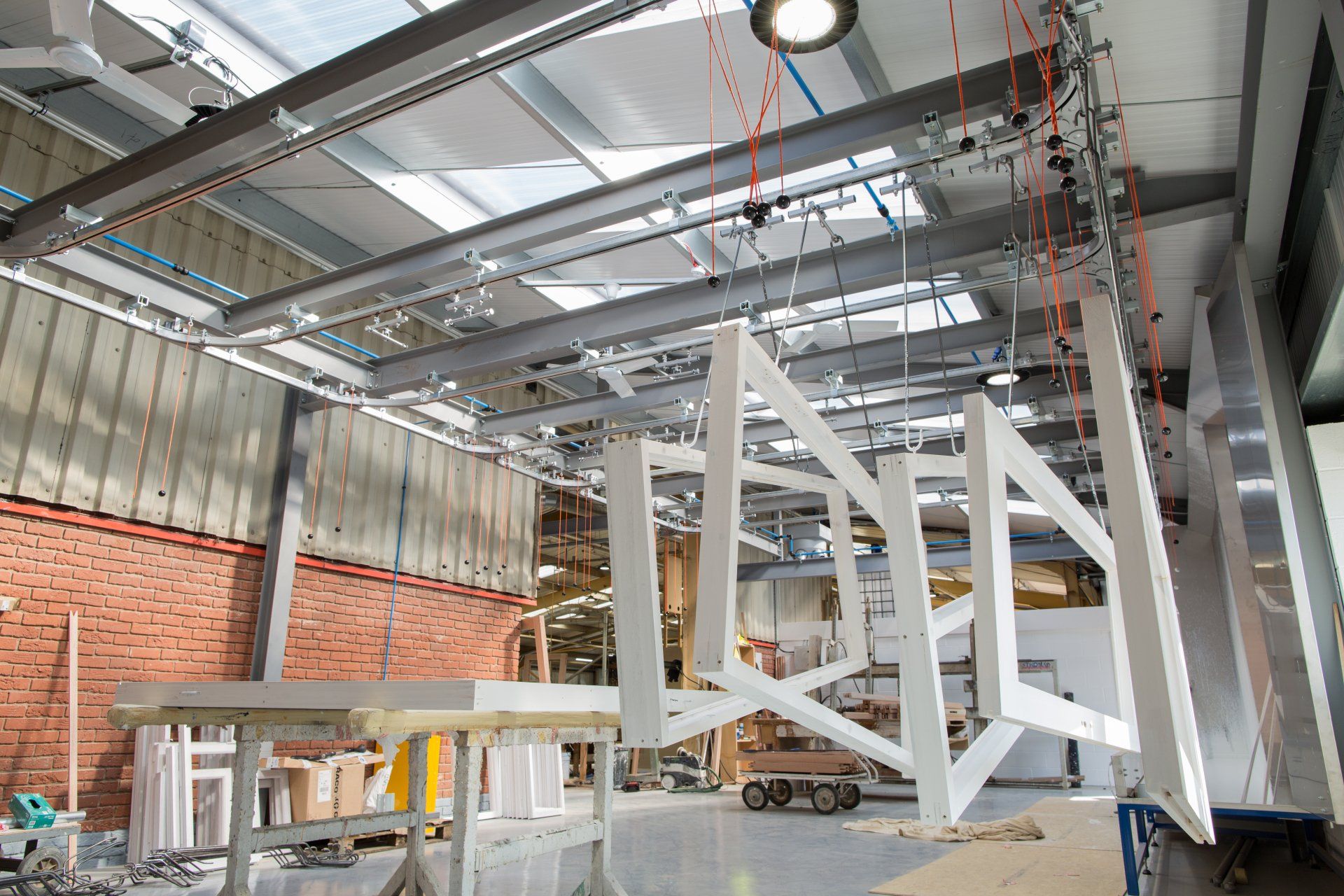 White-painted wooden frames suspended from a conveyor system in a factory.