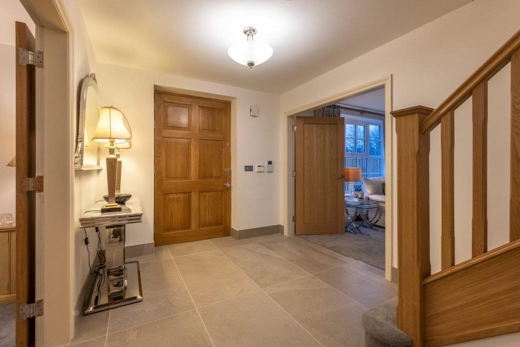 Hallway with light-colored walls, wooden doors, and a decorative table with a lamp. Staircase on the right.