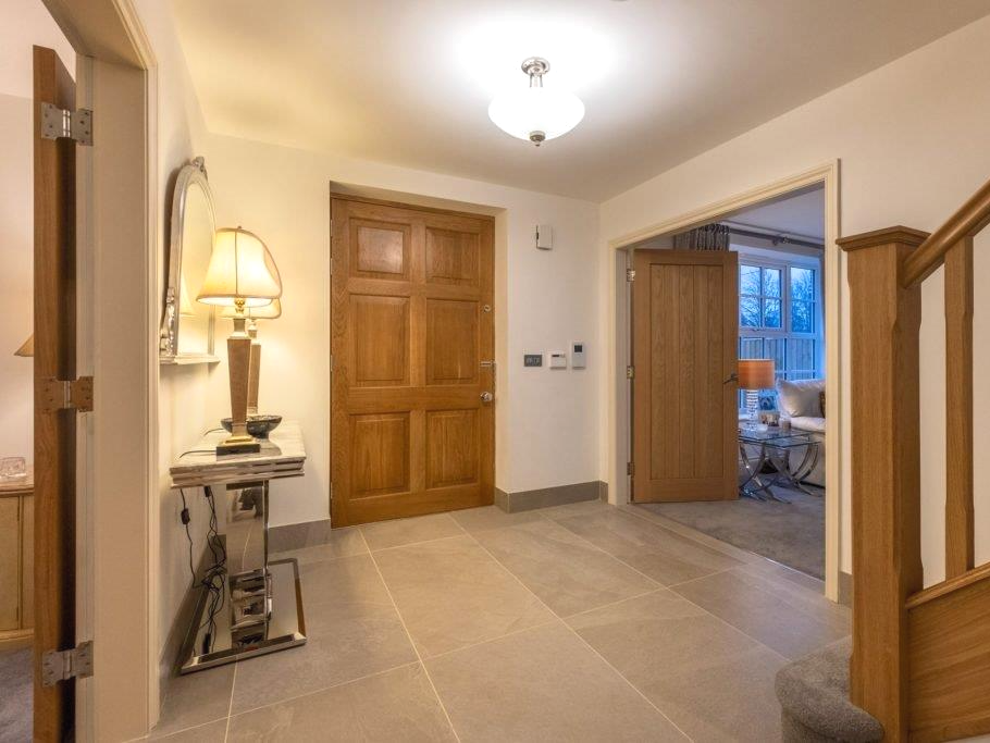 Hallway with a wooden door, side table with lamp, and doorway to a living area.