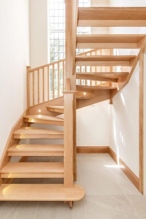 Wooden spiral staircase with natural light, leading to a second floor, built-in lights on the steps.