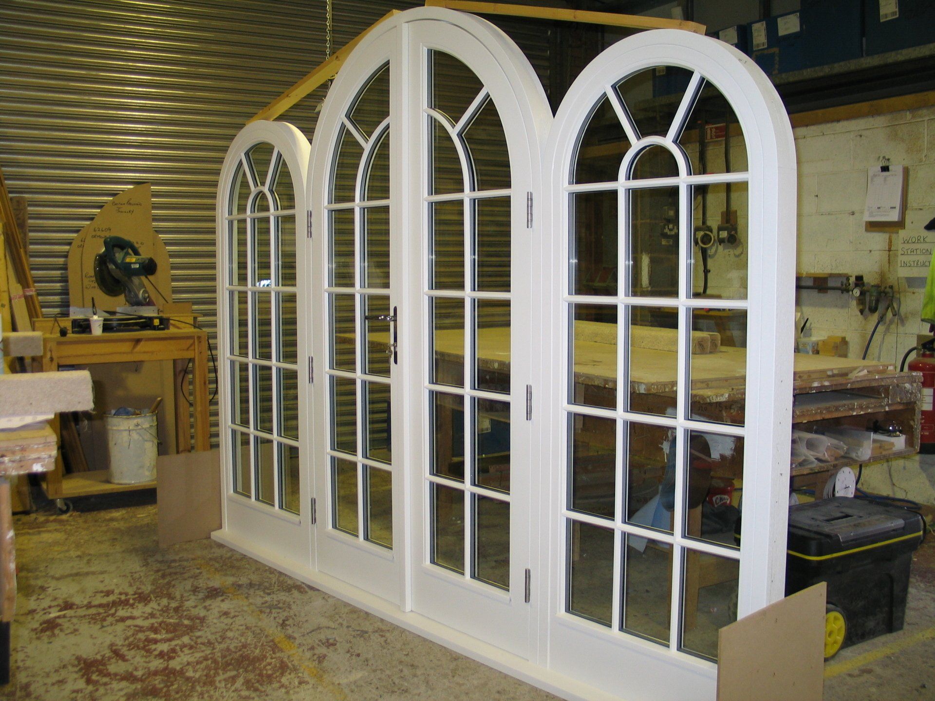 Three white arched French doors in a workshop, ready for installation.