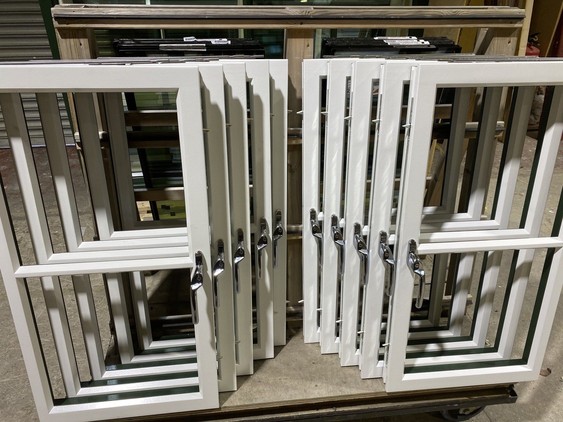 White window frames with glass stacked on a surface, hardware visible.