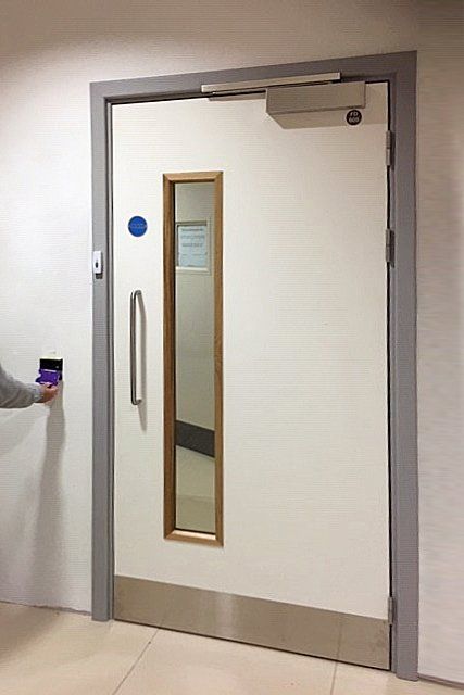 A person uses a purple card reader to open a white door with a narrow window.