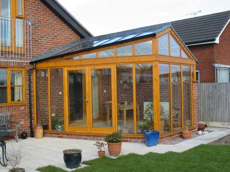 Sunroom addition with wooden frames, glass panels, and brick walls, attached to a red brick house.