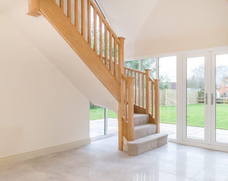 Wooden staircase with carpeted steps, light-colored walls, and a glass door leading to a garden.