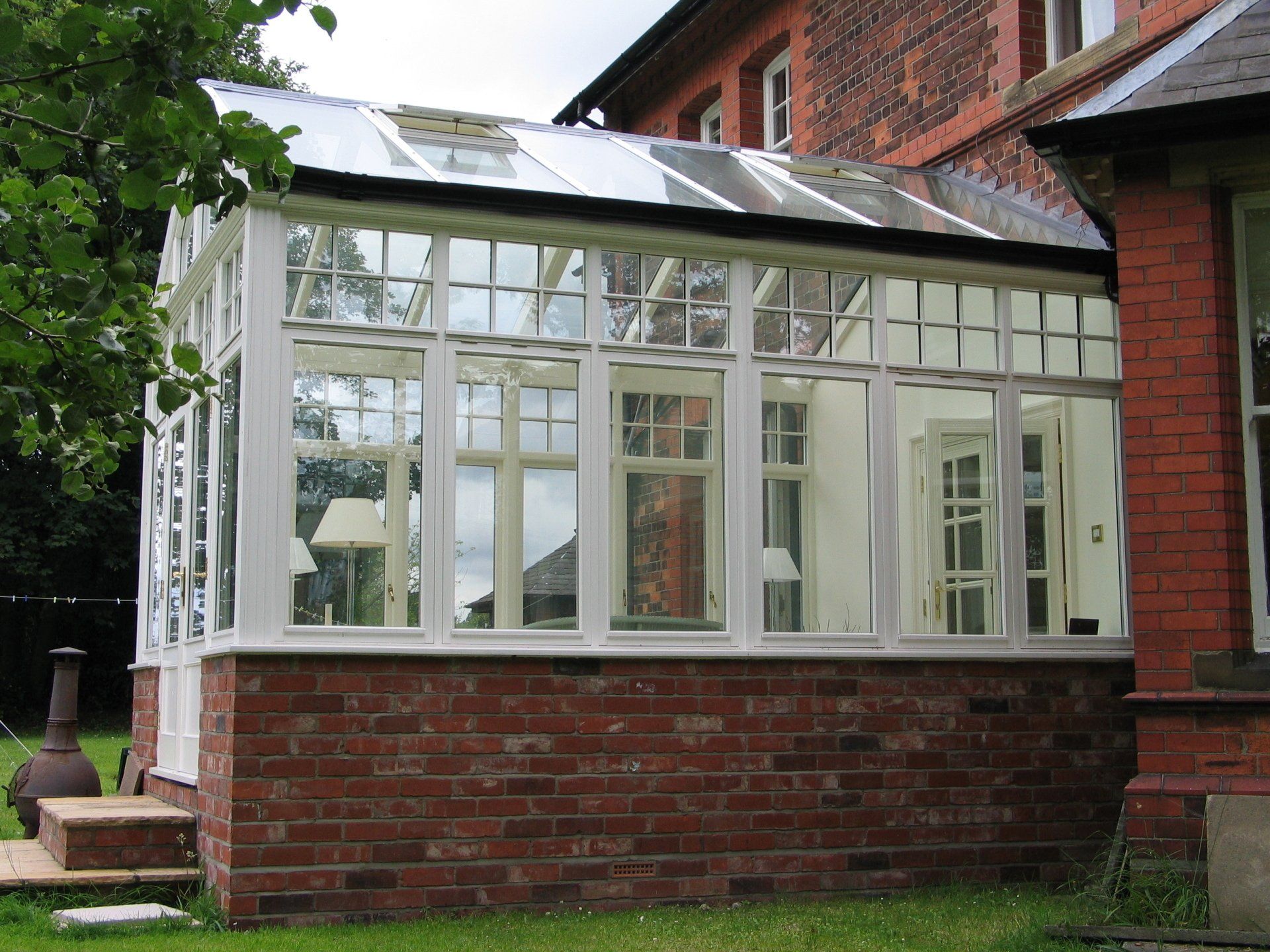 White-wood framed sunroom with glass windows and roof, built onto a red brick building; set outdoors.