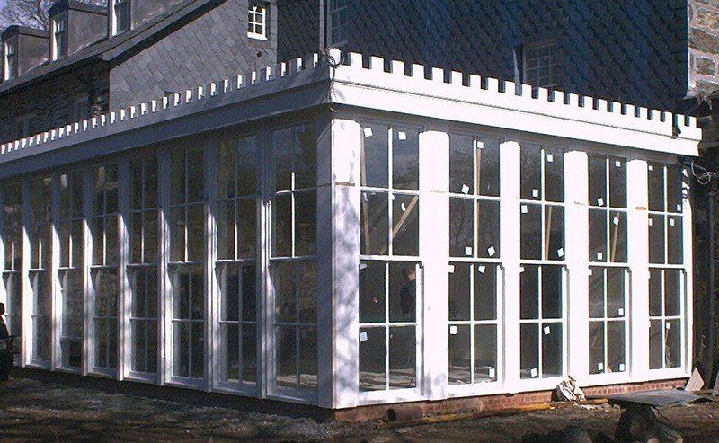 Glass-walled sunroom addition to a stone building. White trim, multiple windows, stone exterior.