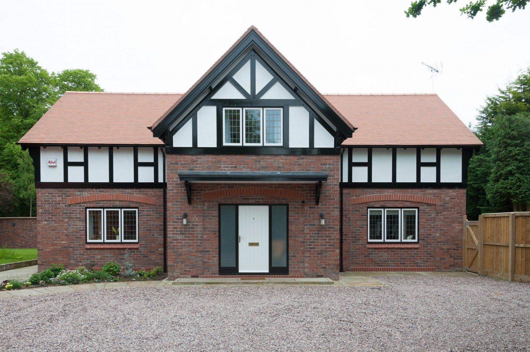 Brick house with a white and black Tudor-style upper story, red tile roof, and gravel drive.