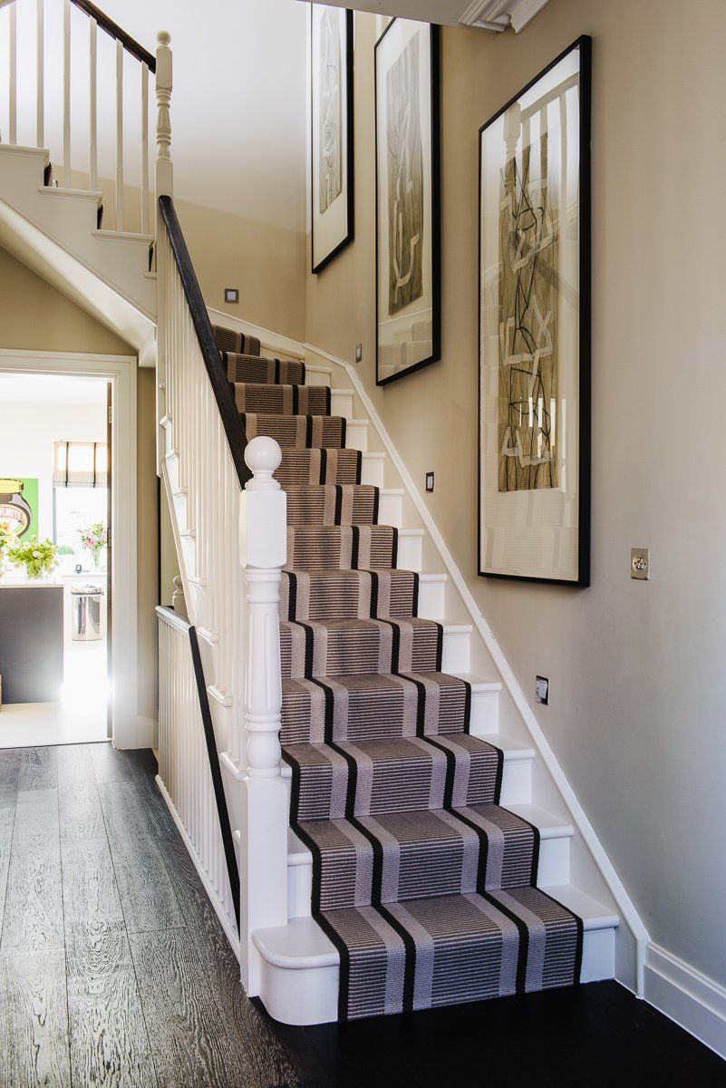 A stairwell with gray carpet runner and white trim, leading to an upper level. Black floorboards and framed art.