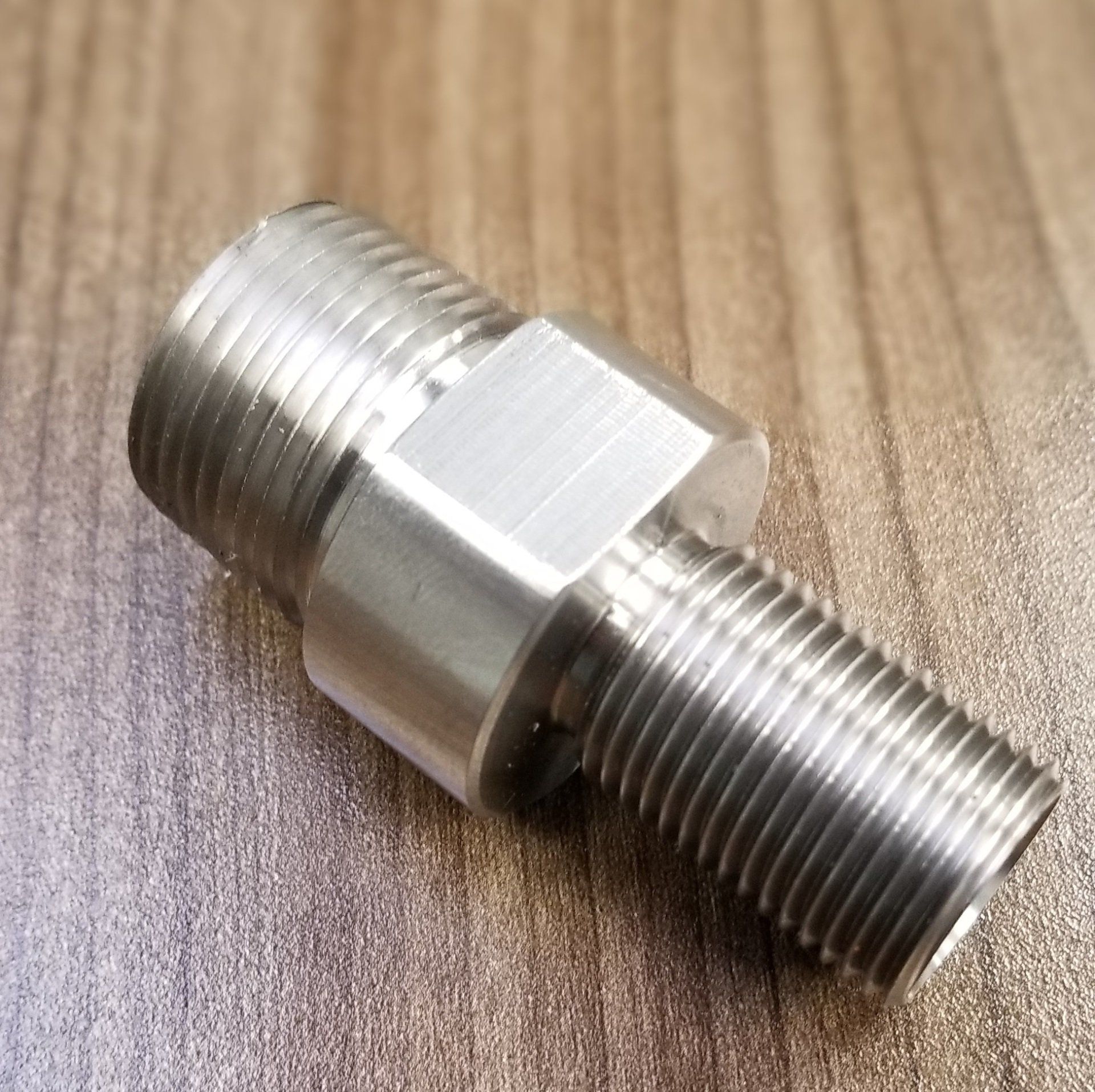 A stainless steel fitting is sitting on a wooden table.