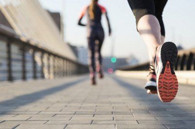 Corredores fazendo jogging em uma calçada pavimentada, com um close do solado de um tênis em primeiro plano.