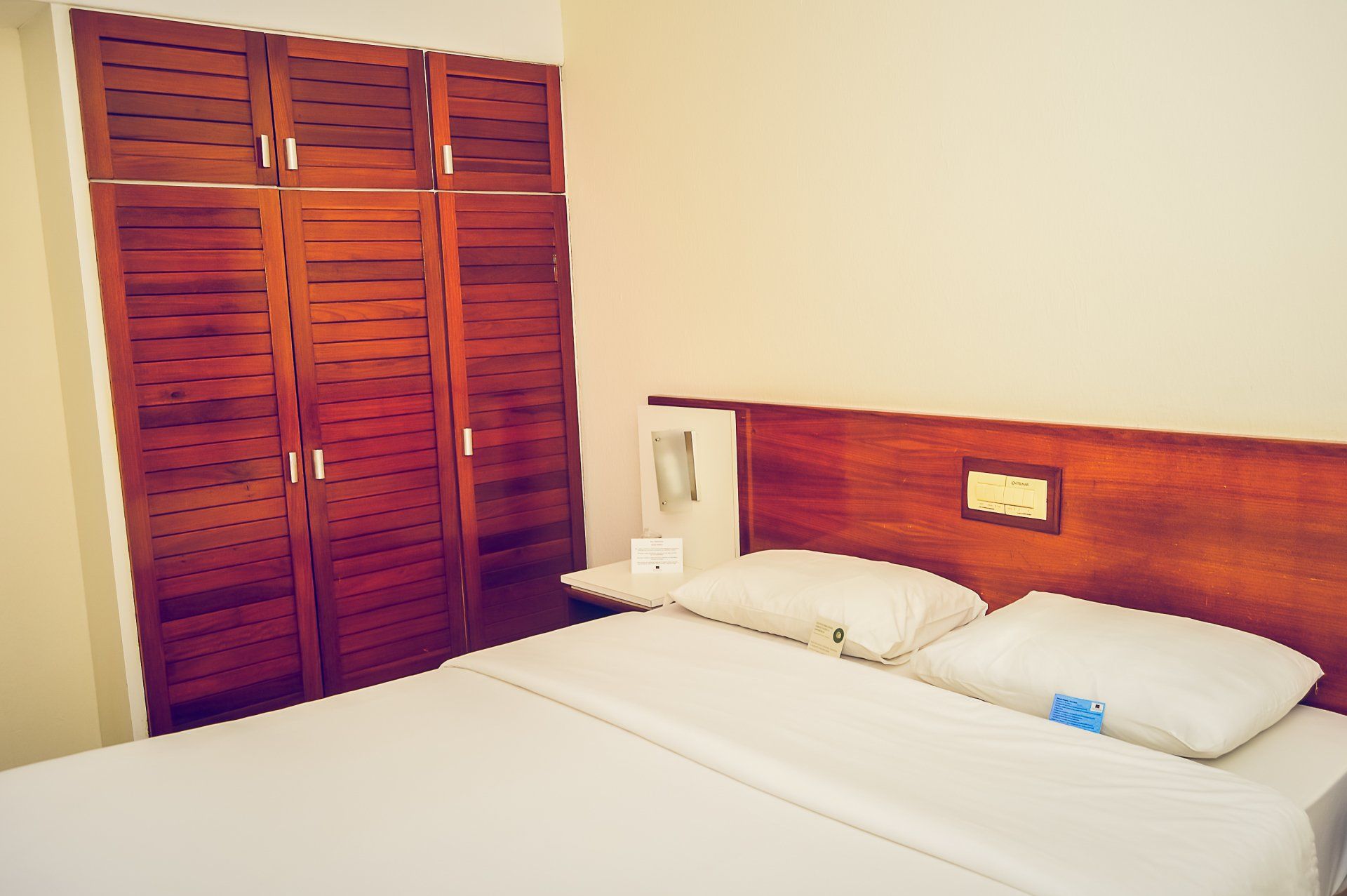 Quarto com cama branca, cabeceira de madeira e portas de armário de madeira.