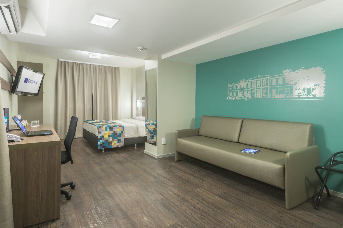 Sala de espera moderna de clínica com parede de destaque em tom azul-petróleo, sofá cinza e área de cama com cortina.