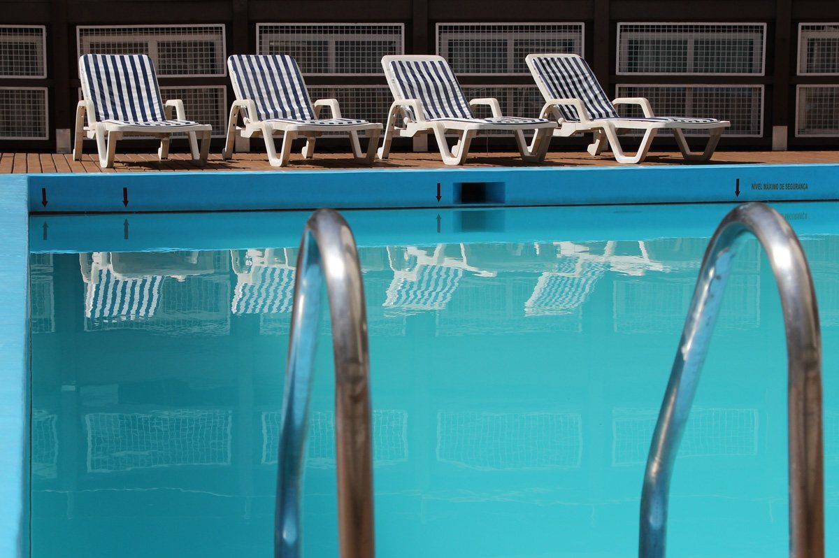 Espreguiçadeiras à beira da piscina azul cristalina com corrimãos em primeiro plano.