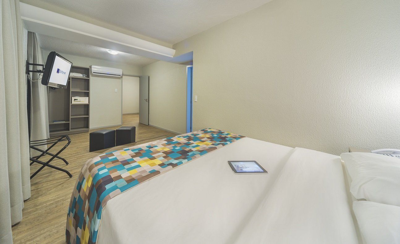 Quarto moderno com cama, cobertor colorido, espelho, guarda-roupa e TV em um suporte.