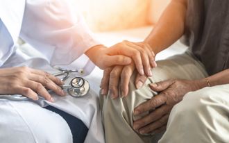 doctor holding stethoscope puts hand on patient's hand