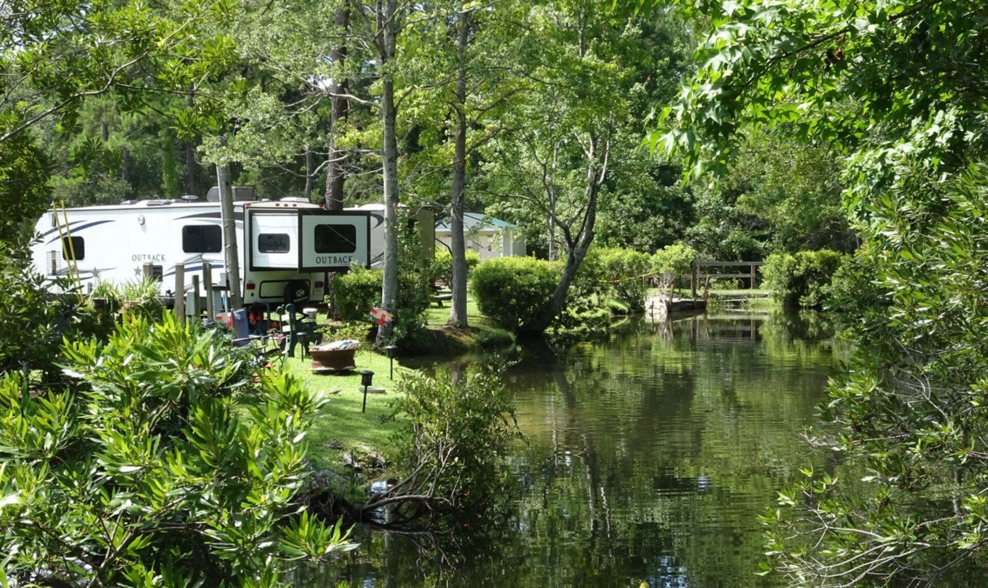 RV parked near pond, surrounded by lush trees.