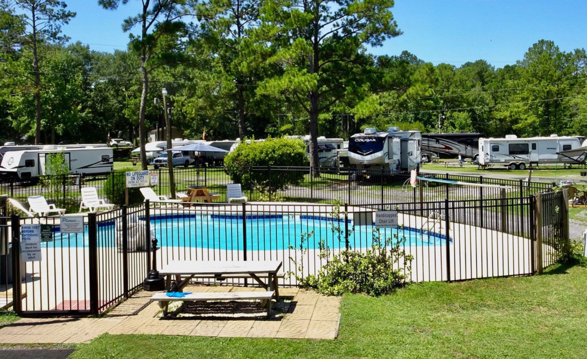 Swimming pool with RVs in the background, surrounded by trees.