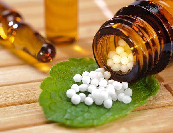 a bottle of homeopathy pills spilling out onto a green leaf.