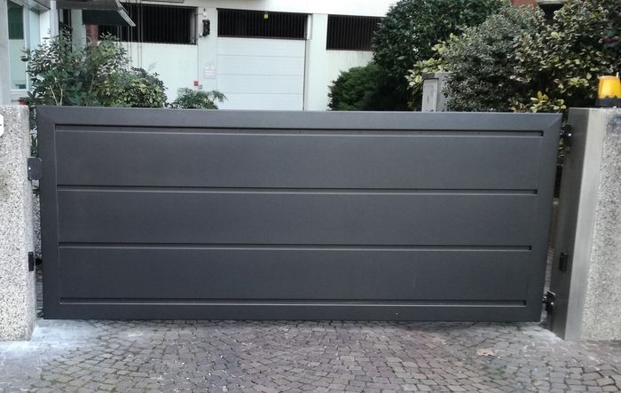 Un cancello nero si trova su un vialetto di ciottoli di fronte a una casa.
