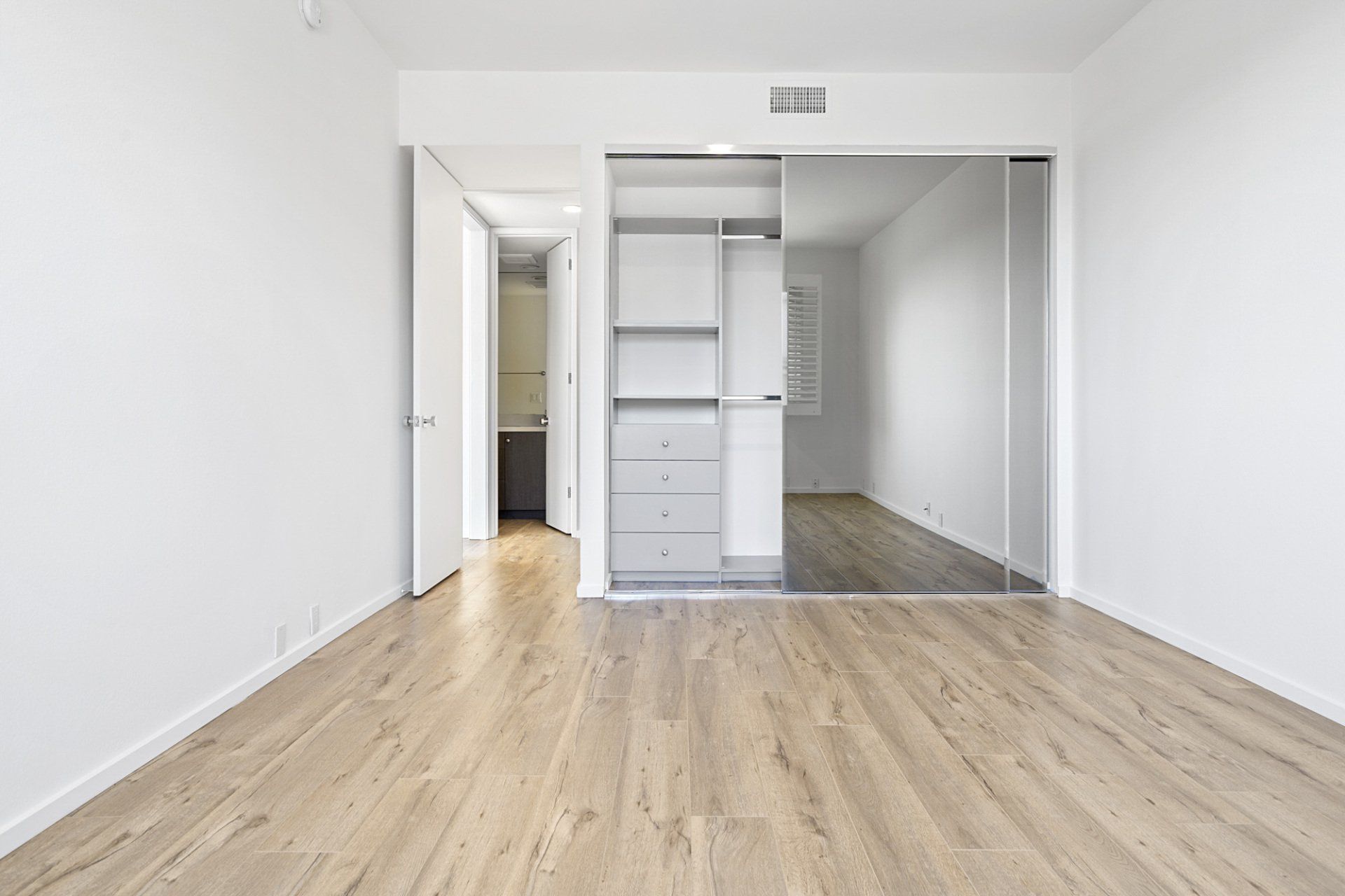 Interior view of bedroom with hardwood floors and a large closet with sliding mirror door