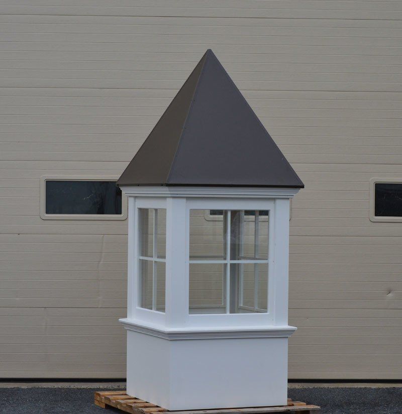 A white building with a brown roof is sitting on a wooden pallet in front of a garage door.