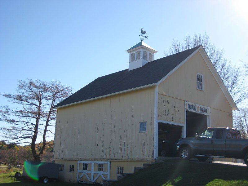 A truck is parked in front of a barn with a weather vane on top