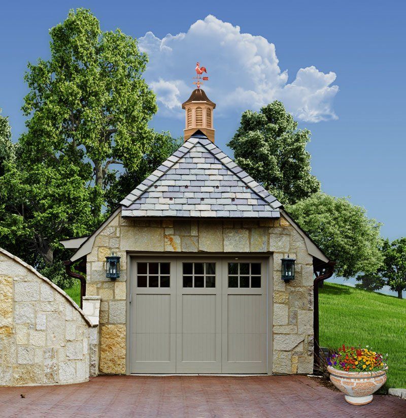A stone garage with a slate roof and a weather vane on top