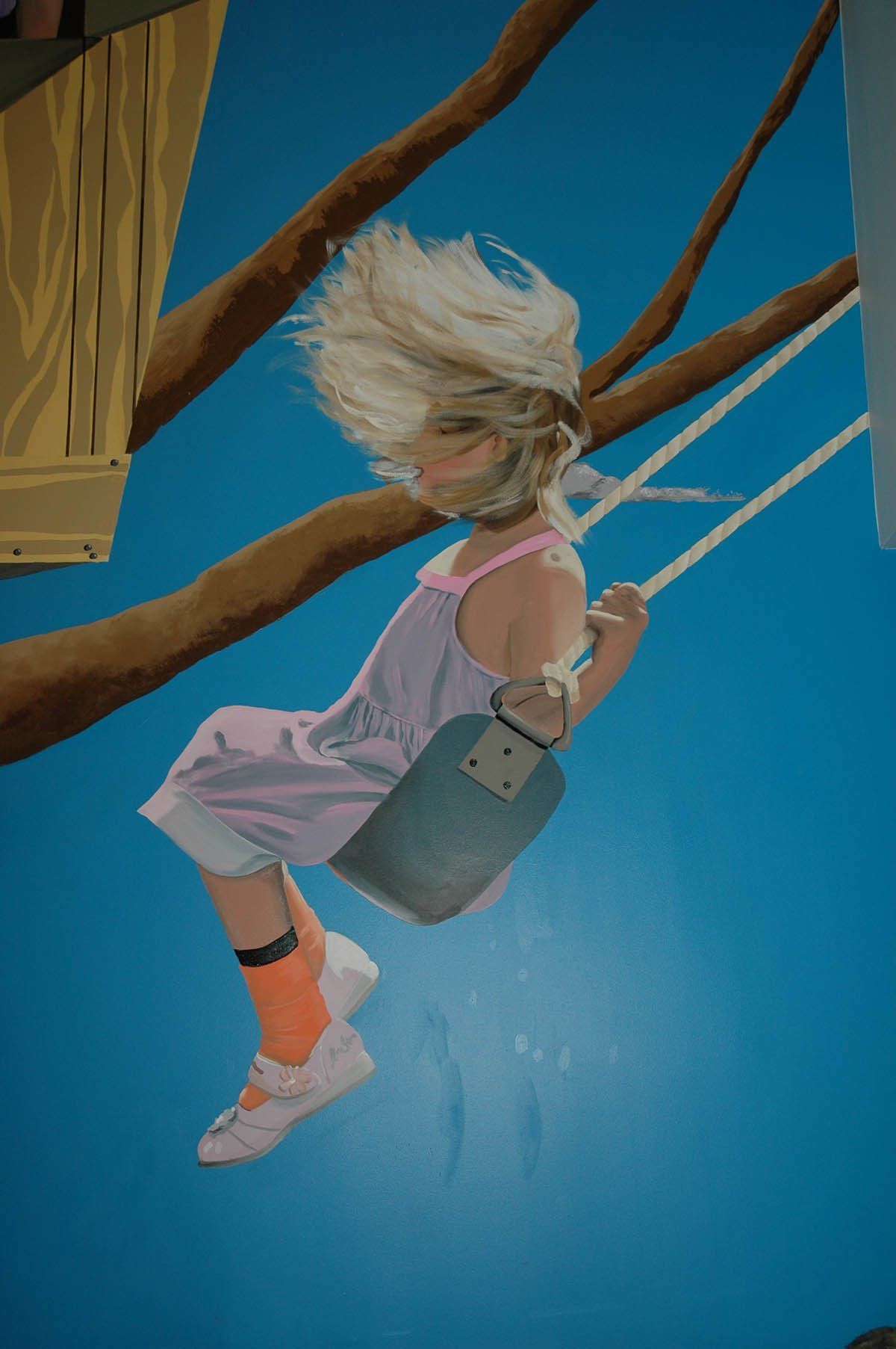 A little girl is sitting on a swing in a tree.