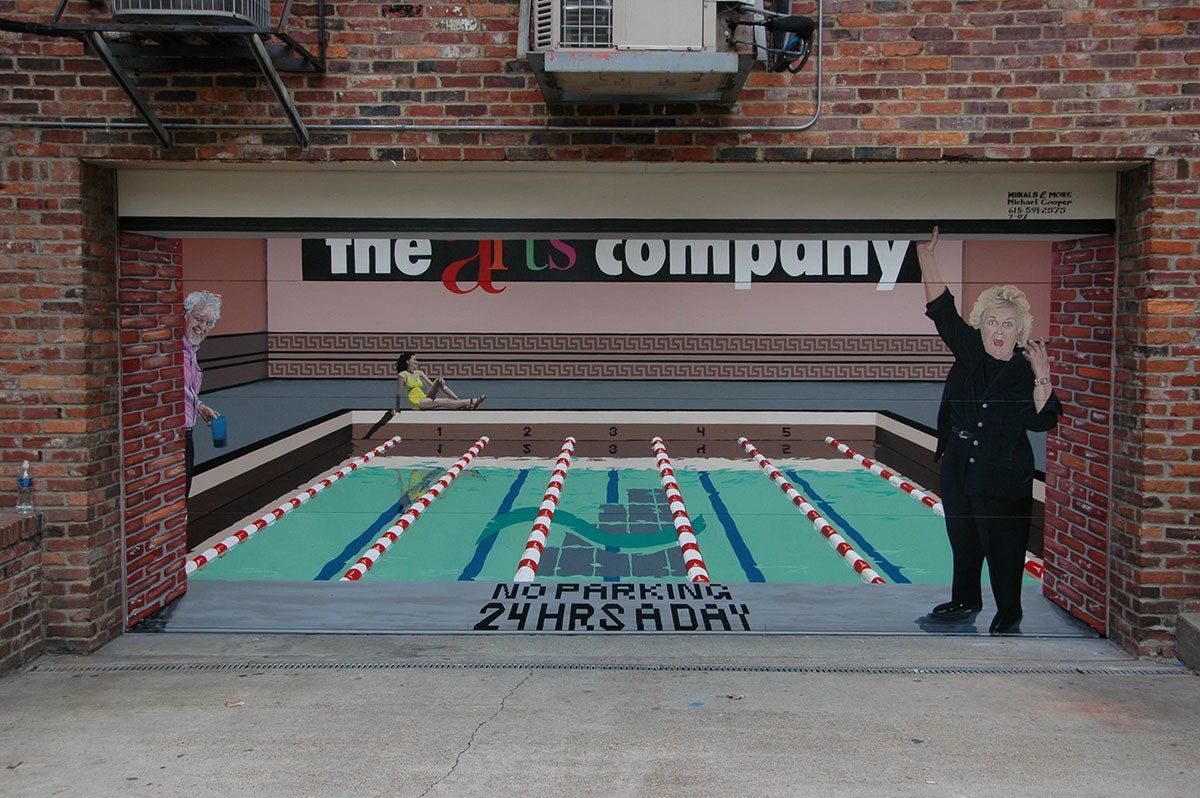 A brick wall with a painting of a pool and a sign that says the arts company