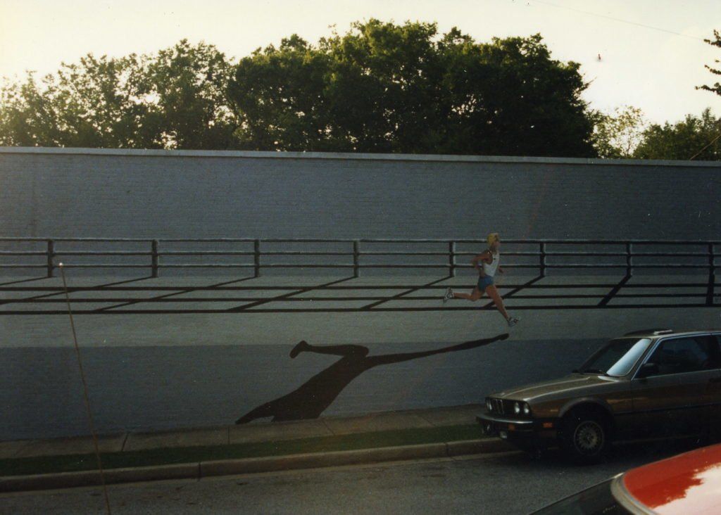 A car is parked in front of a wall with a shadow of a person on it