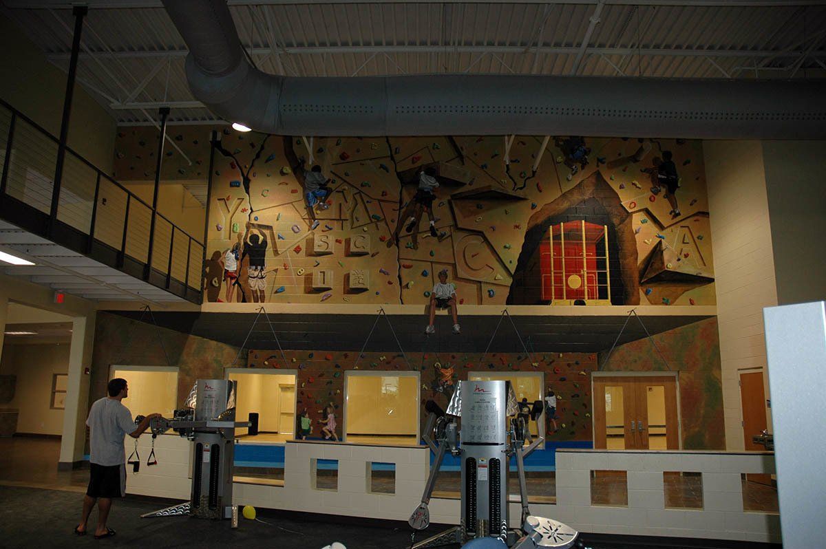 A man is standing in front of a climbing wall in a gym.