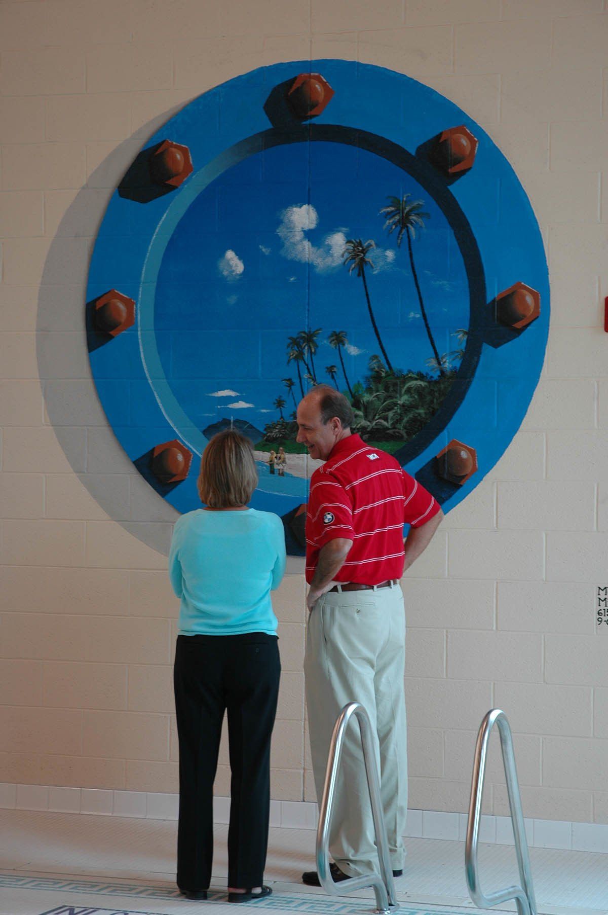 A man and a woman are looking at a painting on a wall