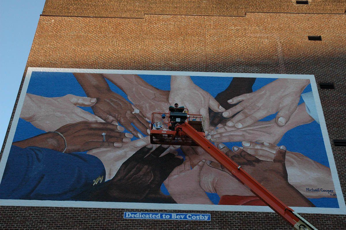 A painting of a group of people holding hands on a brick wall