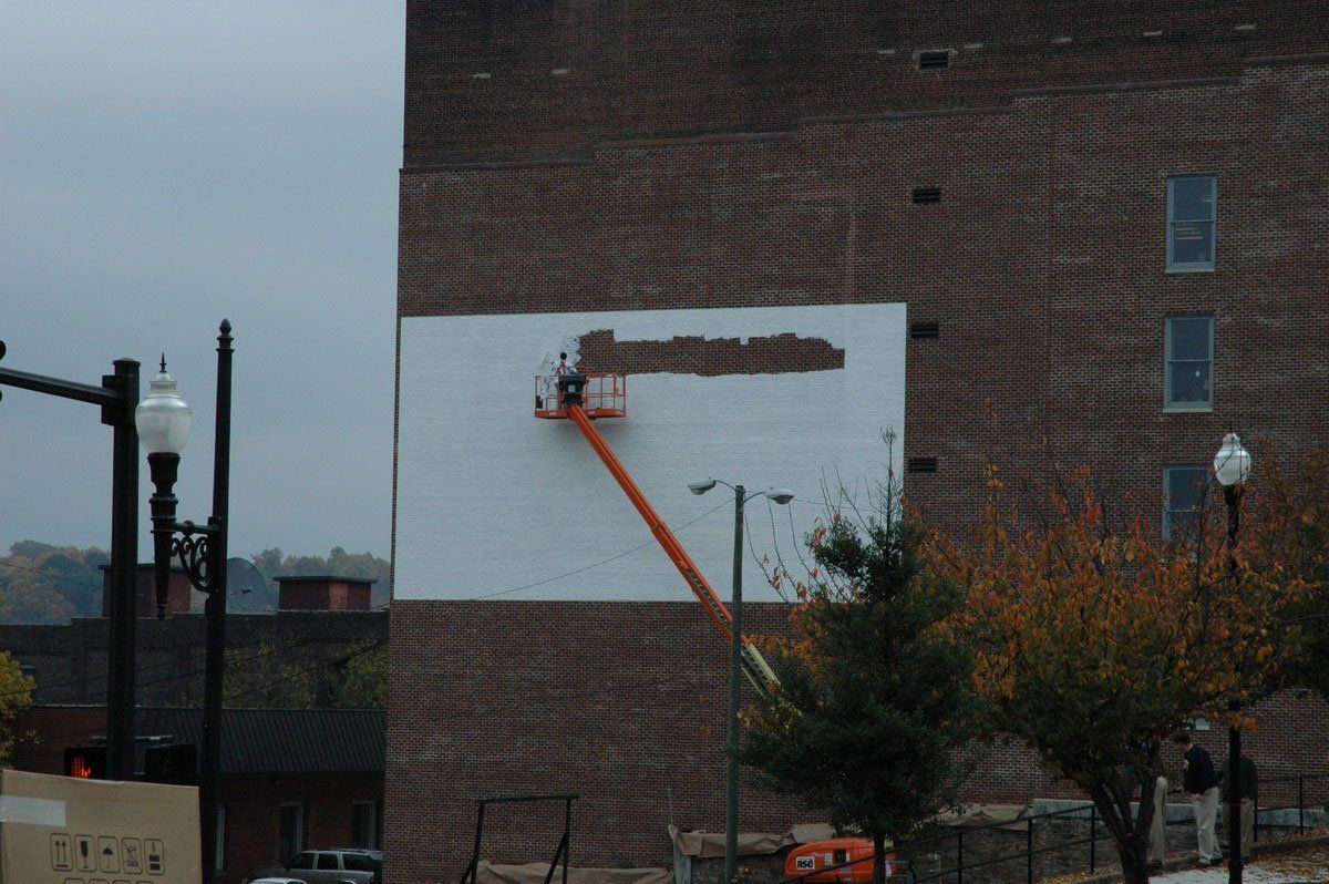 A man is painting a large white sign on the side of a brick building