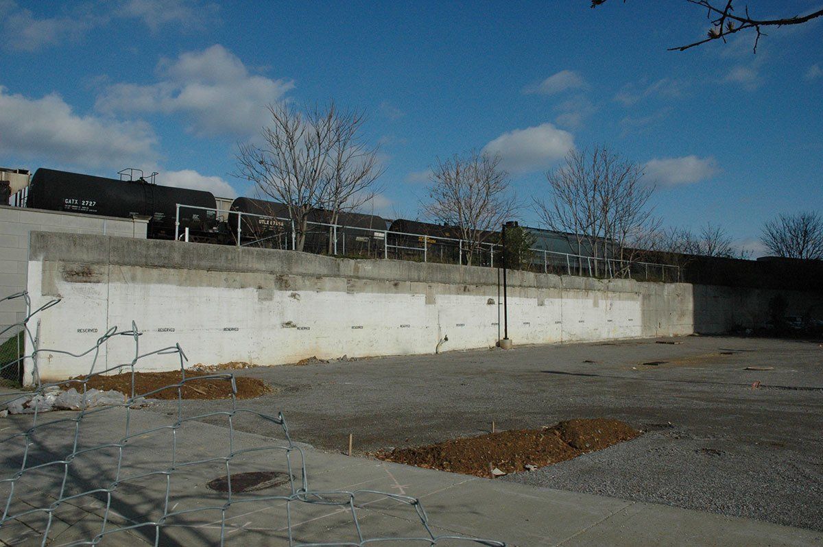 A large white wall is surrounded by gravel and trees